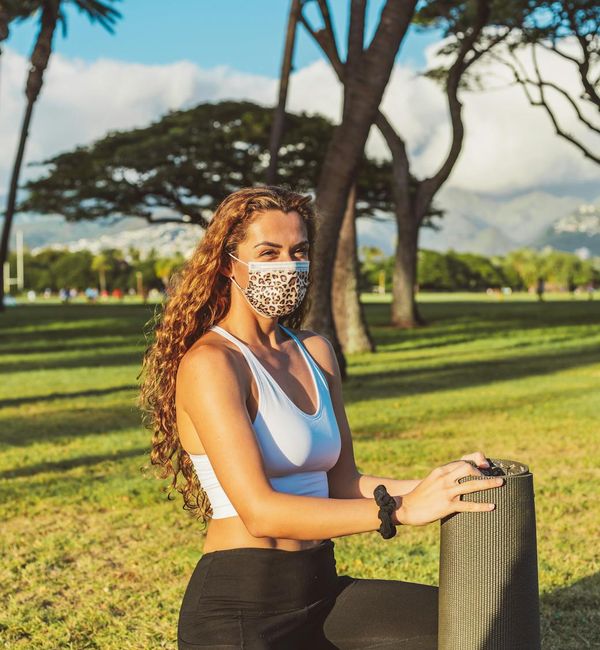 Smiling woman in a bright yoga outfit stretching outdoors.